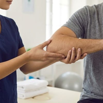 A physiotherapist in a clinic gently examining a patient's arm during an assessment for conditions like Golfer's & Tennis Elbow